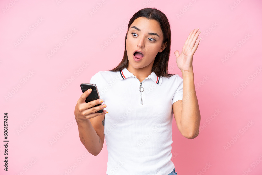 Young caucasian woman isolated on pink background looking at the camera while using the mobile with surprised expression Young caucasian woman isolated on pink background looking at the camera while using the mobile with surprised expression
