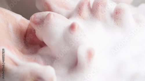 Female hands are washing with soap bubbles. Woman plays with fluffy foam in bathtub, macro. Lady holds handful of soap bubbles, close up.