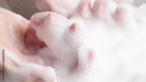 Female hands are washing with soap bubbles. Woman plays with fluffy foam in bathtub, macro. Lady holds handful of soap bubbles, close up. photo