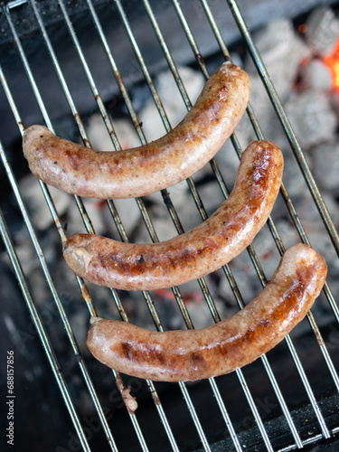 Meat sausages are cooked on a grill over coals