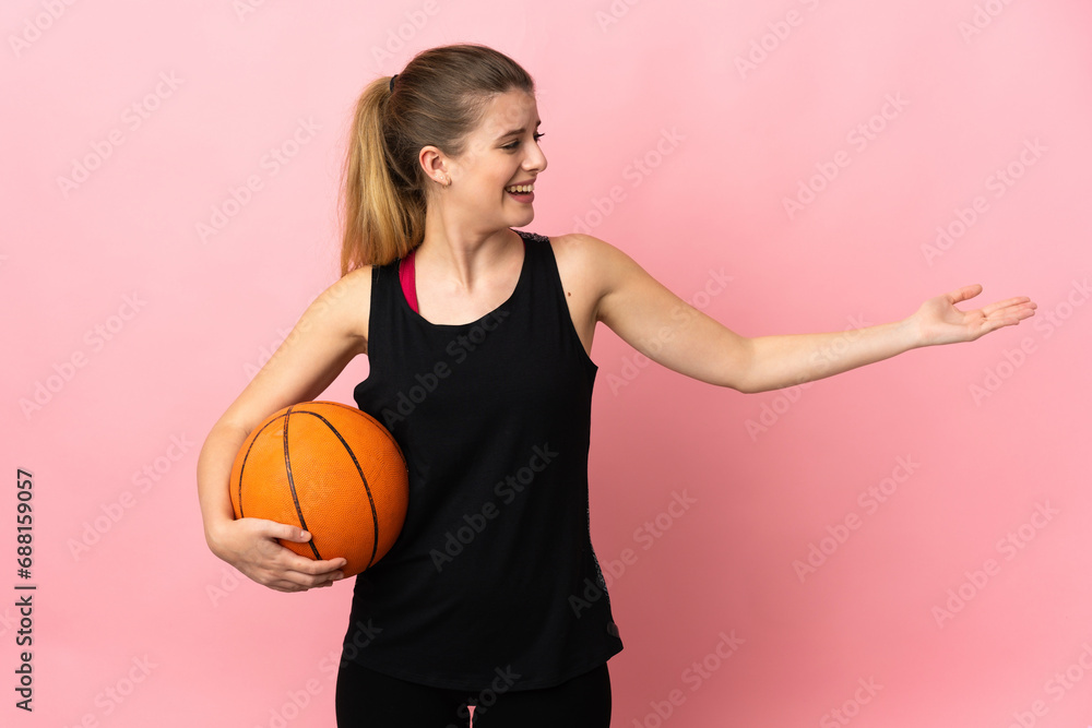 Young blonde woman playing basketball isolated on pink background extending hands to the side for inviting to come