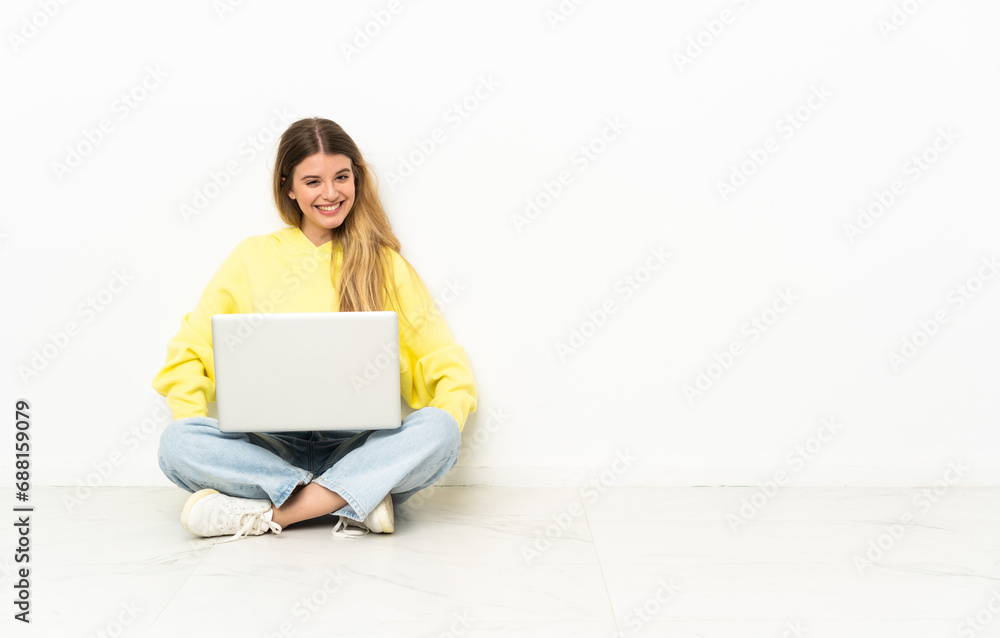 Young woman with a laptop sitting on the floor posing with arms at hip and smiling Young woman with a laptop sitting on the floor posing with arms at hip and smiling