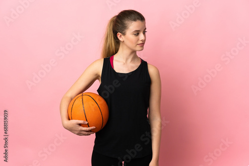 Young blonde woman playing basketball isolated on pink background looking to the side