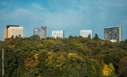 Modern high-rises buildings stick out of dense forest on hill slope