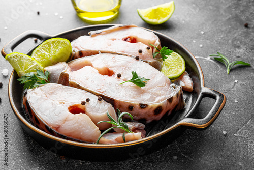 Raw catfish steaks with herbs, lime and spices in a baking dish on a gray background