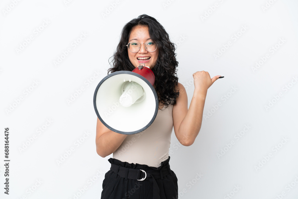 Young asian woman isolated on white background shouting through a megaphone and pointing side Young asian woman isolated on white background shouting through a megaphone and pointing side