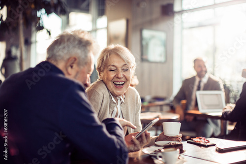 Senior couple sitting in cafe laughing with smartphone photo