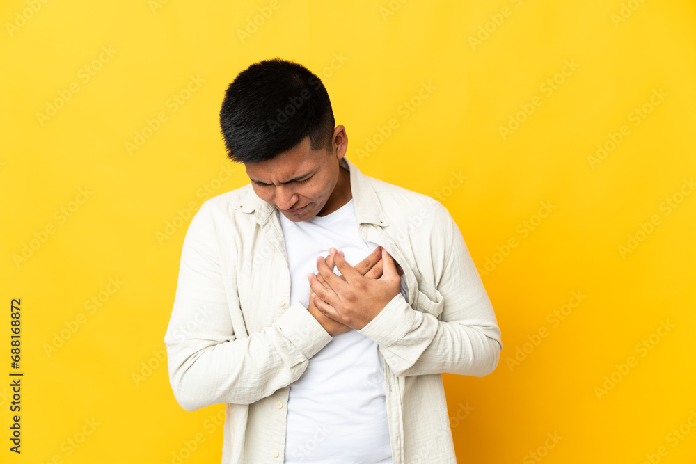 Young Ecuadorian man isolated on yellow background having a pain in the heart Young Ecuadorian man isolated on yellow background having a pain in the heart