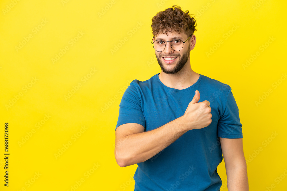 Young handsome caucasian man isolated on yellow background giving a thumbs up gesture Young handsome caucasian man isolated on yellow background giving a thumbs up gesture