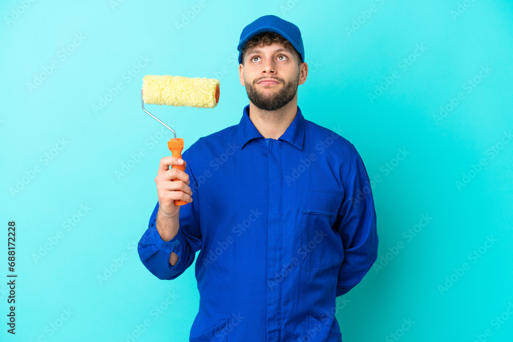 Painter caucasian man isolated on blue background and looking up Painter caucasian man isolated on blue background and looking up