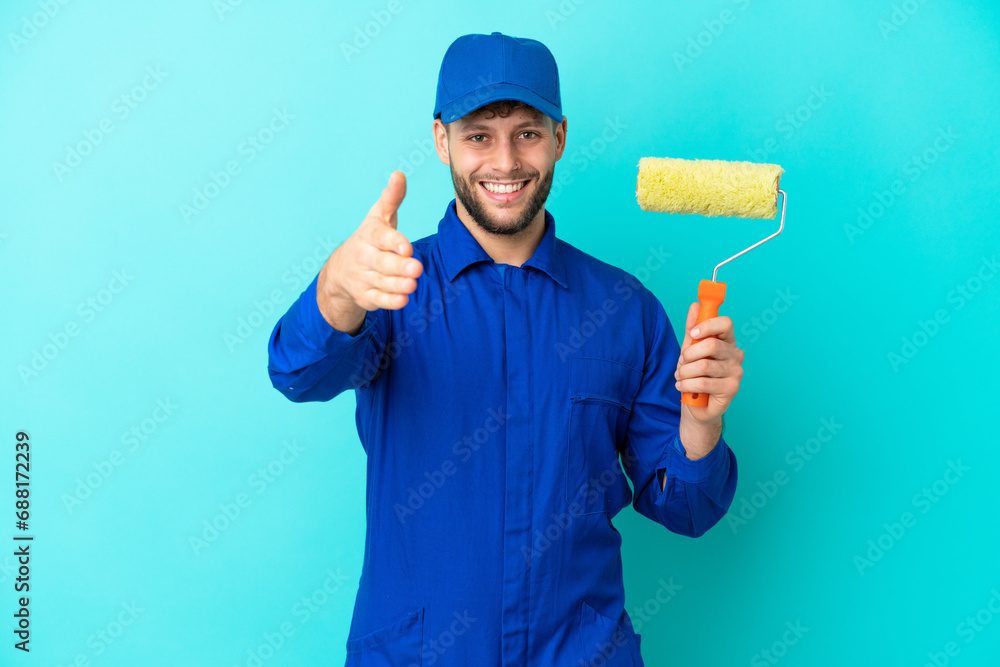 Painter caucasian man isolated on blue background shaking hands for closing a good deal