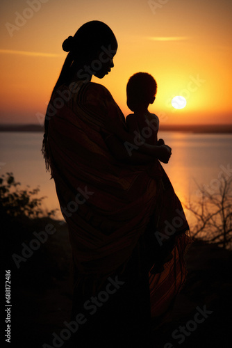 silhouette of a African mother with her child at sunset, in a coastal setting, near the beach. Melancholic sad protective posters love emotions. Beautiful detailed photography.