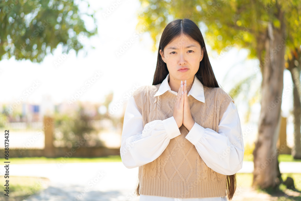 Pretty Chinese woman at outdoors keeps palm together. Person asks for something Pretty Chinese woman at outdoors keeps palm together. Person asks for something