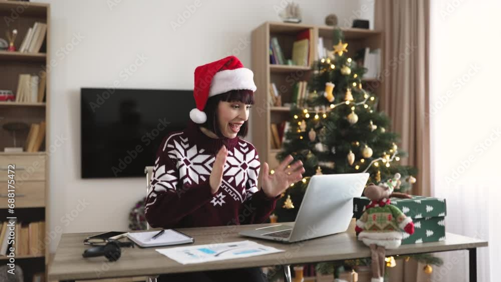 Emotional adult woman in Santa hat and warm winter clothes raising hands with excitement while looking happily at computer screen in living room decorated with Christmas tree. Emotional adult woman in Santa hat and warm winter clothes raising hands with excitement while looking happily at computer screen in living room decorated with Christmas tree.