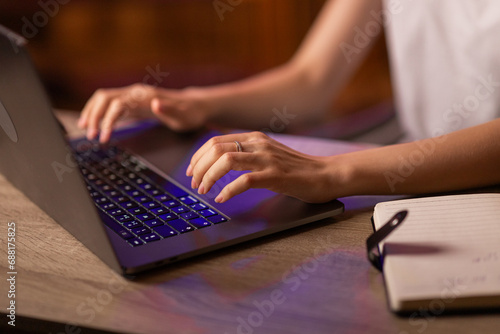 A businesswoman has a job in the office or works at home remotely, sits at the table, uses a copybook for writing notes and laptop for typing text on the keyboard. Close up with no face focused.