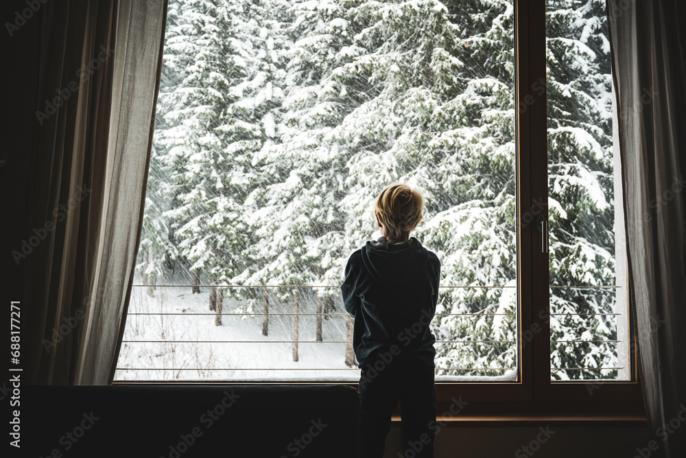 Ein Junge steht am Fenster und beobachtet den Schneefall Ein Junge steht am Fenster und beobachtet den Schneefall