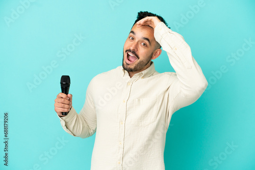Young caucasian singer man isolated on blue background doing surprise gesture while looking to the side © luismolinero