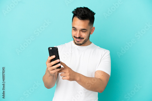 Young caucasian man isolated on blue background sending a message or email with the mobile © luismolinero