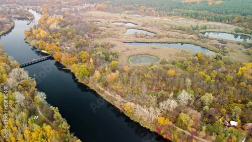 Aerial flying backwards view on bridge across river with autumn trees and recreation area in Korobovy Hutora (Koropove village) in Ukraine photo