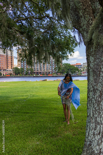 An African American woman with long sisterlocks wearing a colorful dress and sunglasses with green grass and trees along Cape Fear river in Wilmington North Carolina USA