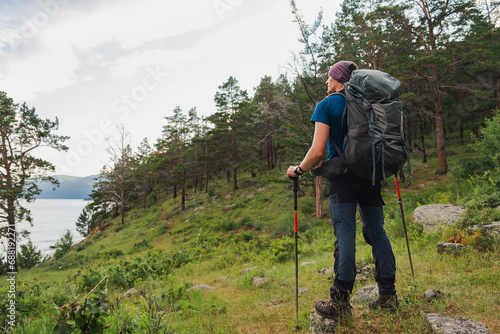 Hiking tourism adventure. Backpacker hiker man looking at beautiful view. Hiker tourist with backpack walking in green forest near lake. Back view man enjoy hike trekking tourism active vacation