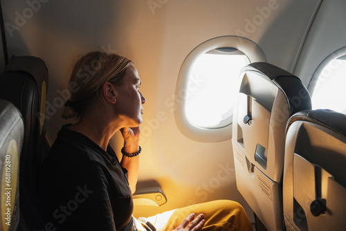 Passenger woman is flying in plane. Girl sitting in airplane looking out window going on trip vacation travel. Traveling female inside plane enjoying flight. Traveling girl