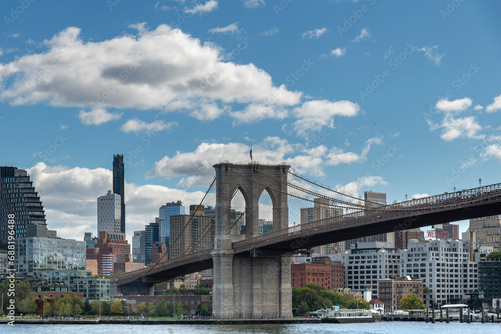 Low angle view from waterfront Lower Manhattan to the Brooklyn Bridge, New York City, USA with Brooklyn Heights with Brooklyn Bridge Park in background 
