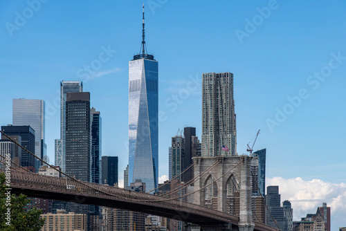 Low angle view from waterfront Brooklyn Bridge Park to the Brooklyn Bridge in Lower Manhattan, New York City, USA with skyscrapers of Lower Manhattan, Two Bridges and Financial district in background