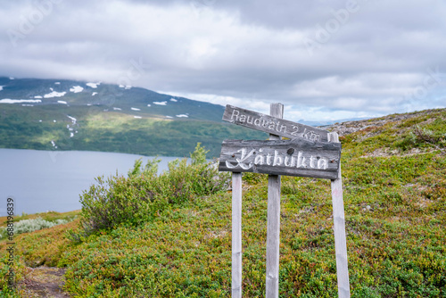 Mountain hiking information sign in Norwegian mountains - the name of current place and distance to the next one. Blurry mountains and lake on background. Close up photo