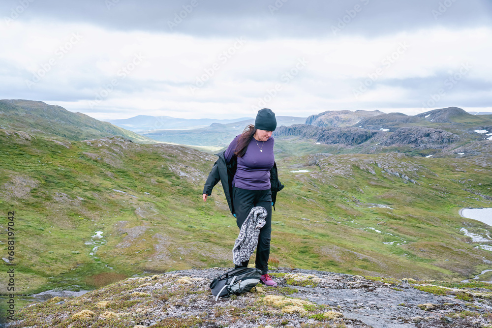 Mature woman is going to dress up with warmer clothes, hiking at high altitude cold high altitude Norwegian Mountains range terrain. Hiking high in Norwegian mountains. Norway, Krutvatnet. Front view