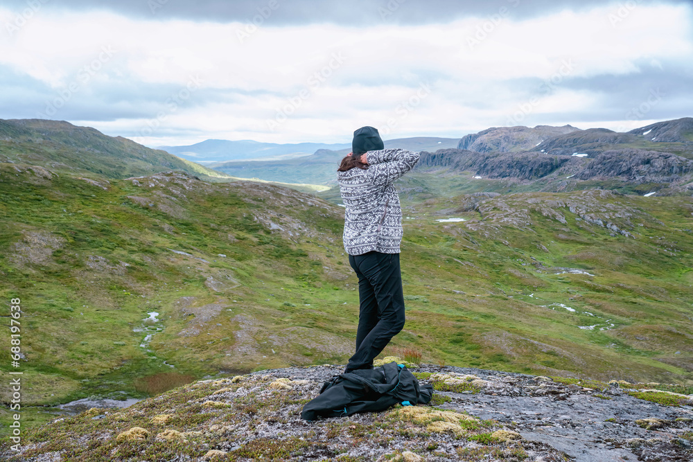 Mature woman adjusts warmer clothes, hiking at high altitude cold Norwegian Mountains range terrain. Hiking high in Norwegian mountains. Norway, Krutvatnet. Side view Mature woman adjusts warmer clothes, hiking at high altitude cold Norwegian Mountains range terrain. Hiking high in Norwegian mountains. Norway, Krutvatnet. Side view