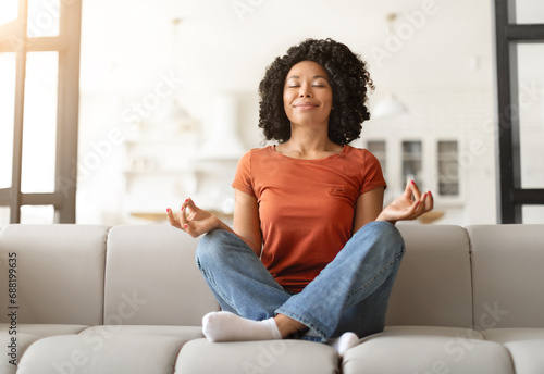 Stress Relief Concept. Peaceful young black woman sitting cross-legged on couch