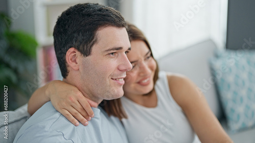 Beautiful couple sitting on sofa hugging each other smiling at home