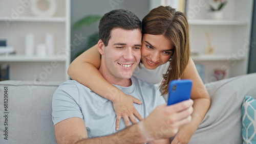 Beautiful couple hugging each other using smartphone smiling at home