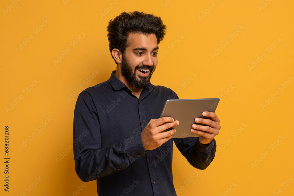Happy young indian man playing online games on digital tablet Happy young indian man playing online games on digital tablet