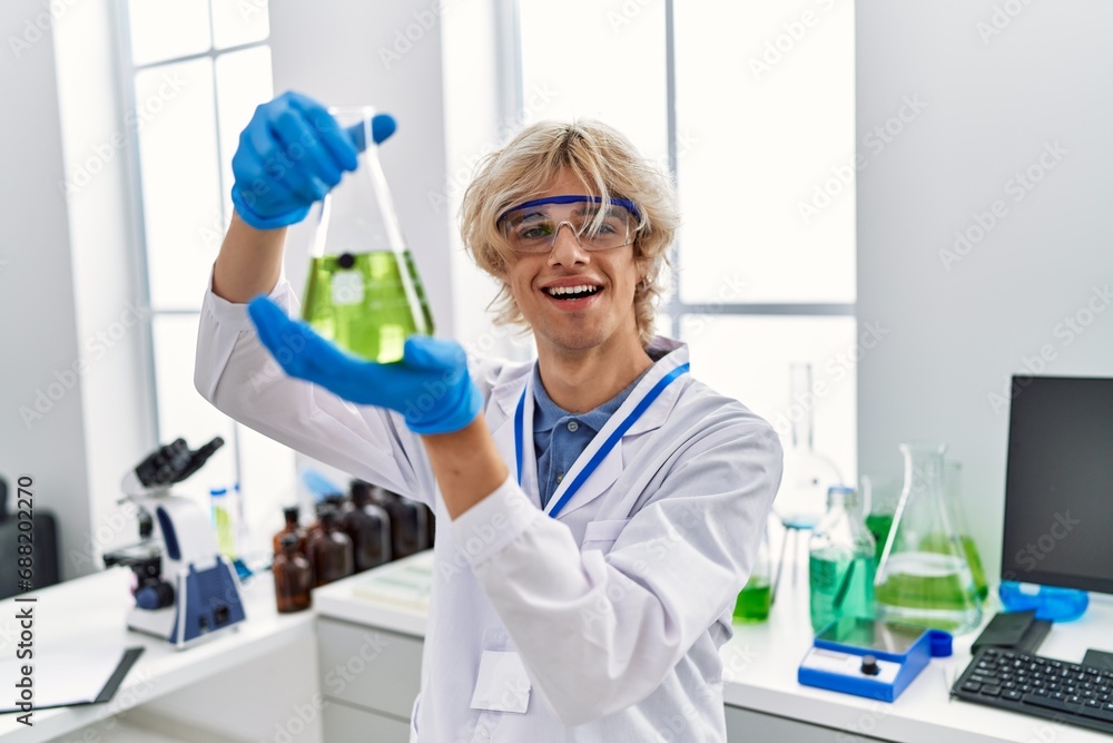 Young blond man scientist smiling confident holding test tube at laboratory