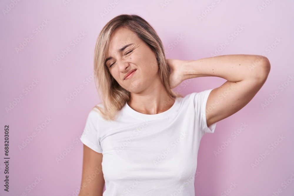 Young blonde woman standing over pink background suffering of neck ache injury, touching neck with hand, muscular pain Young blonde woman standing over pink background suffering of neck ache injury, touching neck with hand, muscular pain