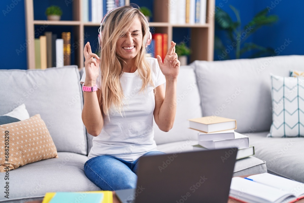 Young blonde woman studying using computer laptop at home gesturing finger crossed smiling with hope and eyes closed. luck and superstitious concept. Young blonde woman studying using computer laptop at home gesturing finger crossed smiling with hope and eyes closed. luck and superstitious concept.