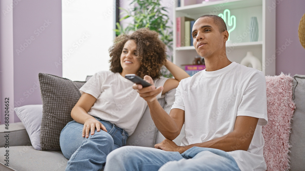 Beautiful couple joyfully watching their favorite film, sitting on the couch at home, sharing smiles and a laugh Beautiful couple joyfully watching their favorite film, sitting on the couch at home, sharing smiles and a laugh