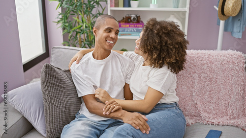 Beautiful couple sitting on sofa, hugging with radiant smiles in their cozy home. a testament of love, an expression of joy and confidence reigns in the room as their casual lifestyle shines through. © Krakenimages.com