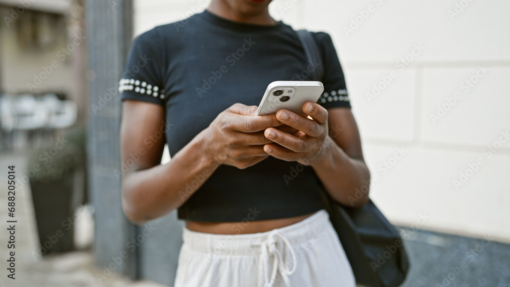 Attractive african american woman engrossed in digital conversation, using her phone outdoors, touching the screen to text in an urban city street setting. Attractive african american woman engrossed in digital conversation, using her phone outdoors, touching the screen to text in an urban city street setting.