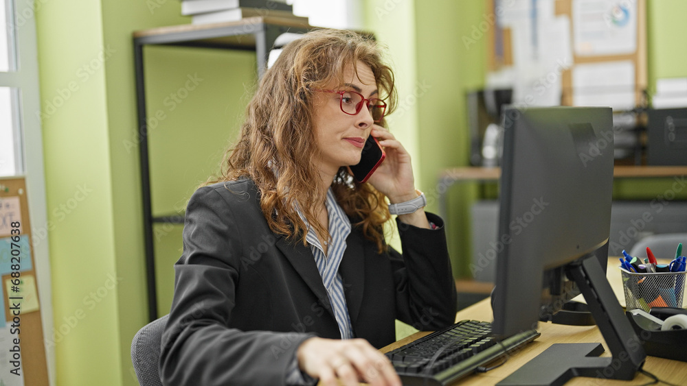 Young woman business worker using computer talking on smartphone at the office Young woman business worker using computer talking on smartphone at the office