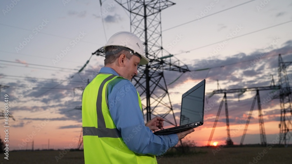 Mature manager sets up power transmission lines equipment via laptop in evening