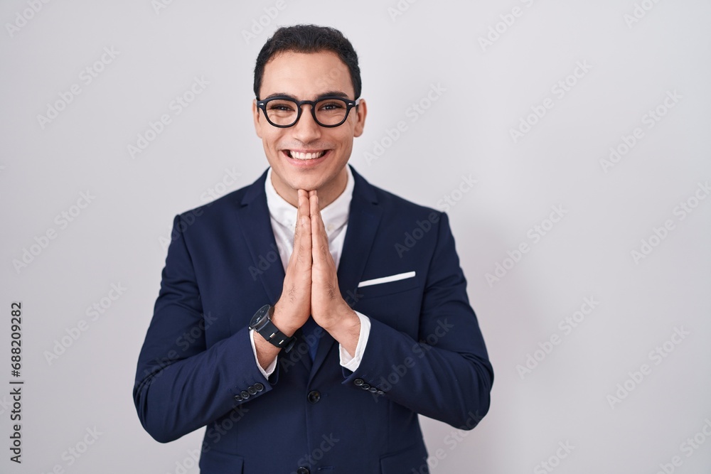 Young hispanic man wearing suit and tie praying with hands together asking for forgiveness smiling confident. Young hispanic man wearing suit and tie praying with hands together asking for forgiveness smiling confident.