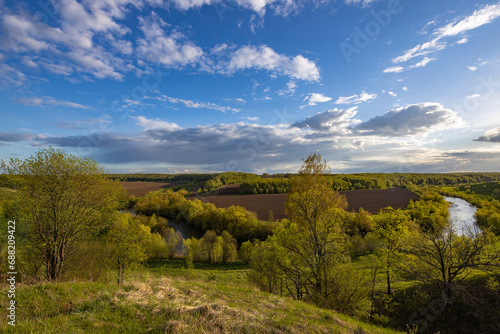 View from the hill to plowed farmland. Landscape with a river  arable land and green trees.