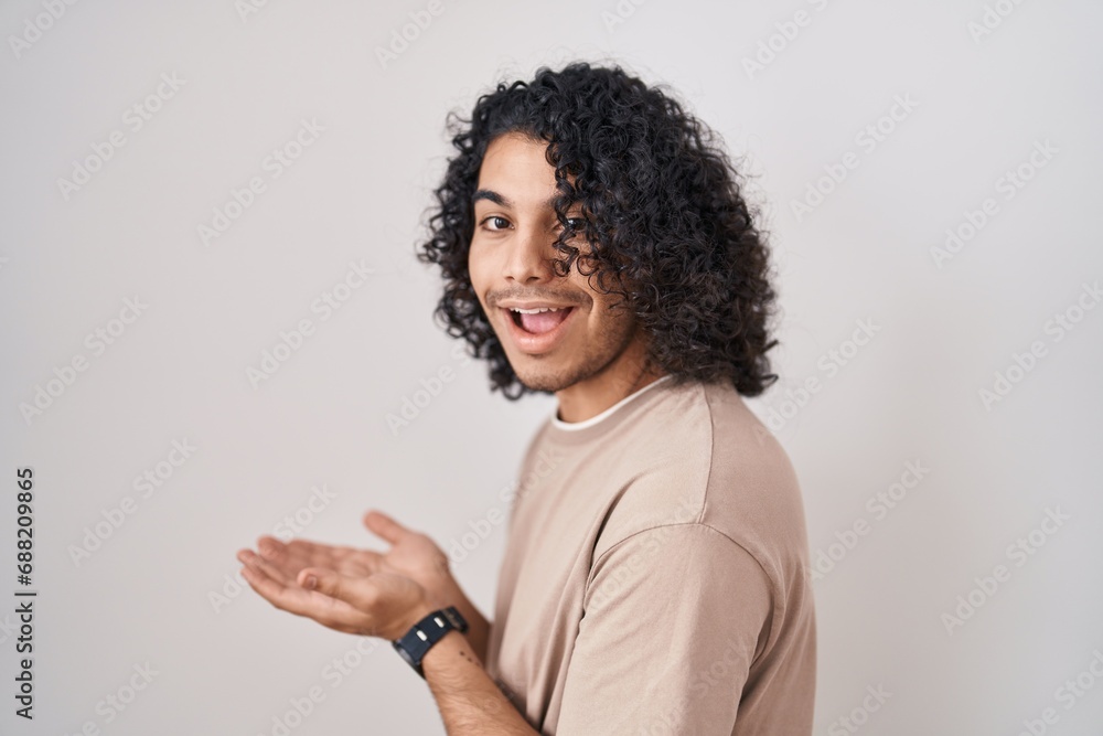 Hispanic man with curly hair standing over white background pointing aside with hands open palms showing copy space, presenting advertisement smiling excited happy Hispanic man with curly hair standing over white background pointing aside with hands open palms showing copy space, presenting advertisement smiling excited happy