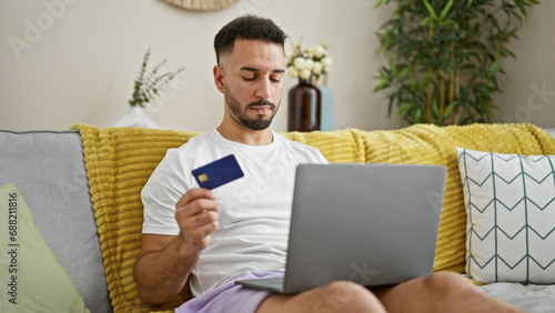 Young arab man shopping with laptop and credit card sitting on sofa at home