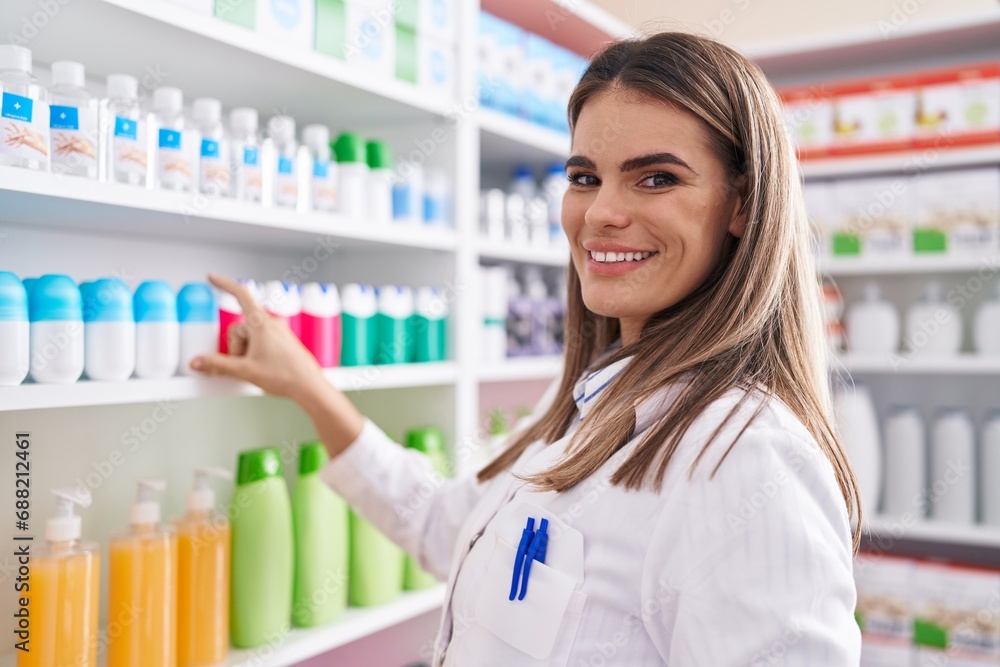 Young beautiful hispanic woman pharmacist smiling confident holding product on shelving at pharmacy