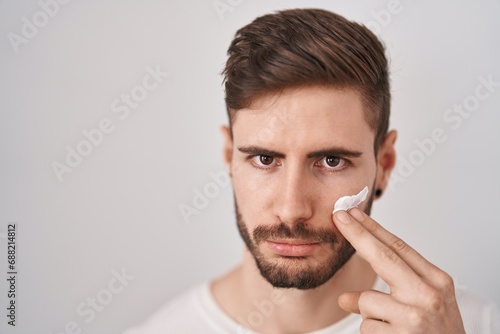Hispanic man with beard using moisturizer facial cream depressed and worry for distress, crying angry and afraid. sad expression.