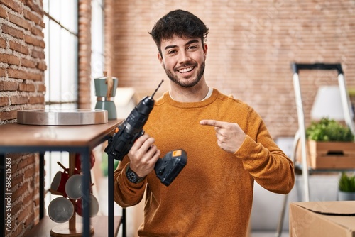 Hispanic man with beard holding screwdriver at new home smiling happy pointing with hand and finger